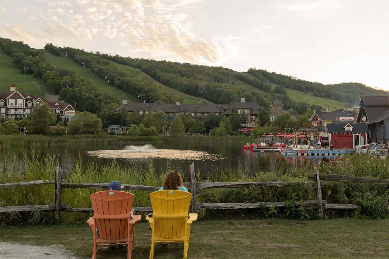 A Mother and her son sit on muskoka chairs over looking Blue Mountain Village. 