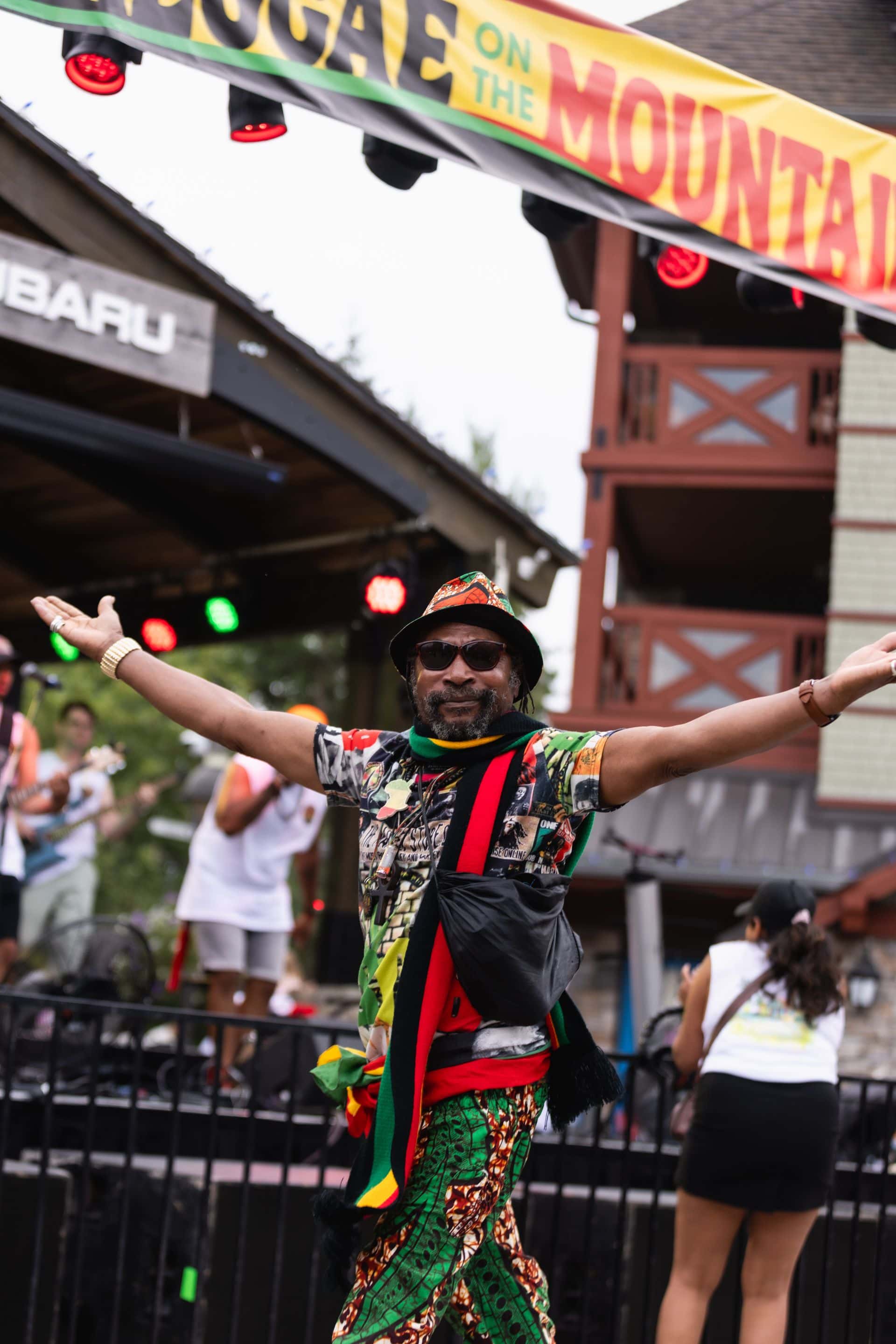 A guest dressed in a full reggae-inspired outfit posing in front of the Subaru Stage during Reggae On The Mountain 2025.