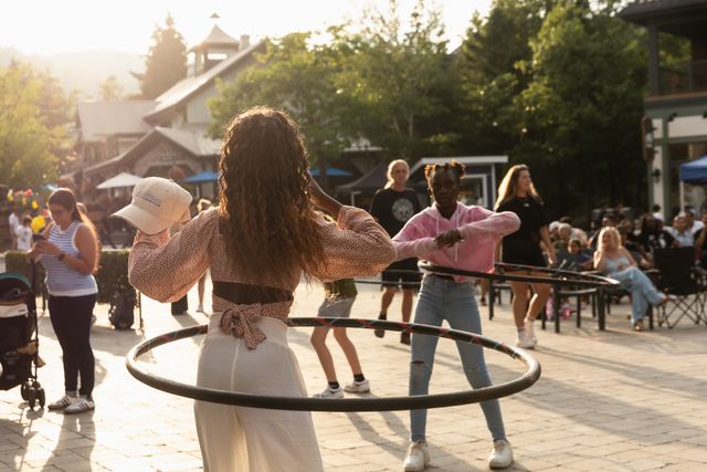 Family challenging each other to hula hoop the longest on a sunny day in the Village Events Plaza.